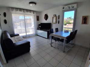 A living room with a sofa, a dining table with chairs, a TV, and a sliding glass door to the outside. - Air-conditioned 2-room apartment with a terrace, a 3-minute walk from the beach and restaurants (Cagnes-sur-Mer)