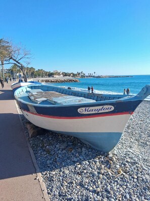A boat named 'Mauflou' on a pebbled beach with a clear blue sky and calm sea. - Air-conditioned 2-room apartment with a terrace, a 3-minute walk from the beach and restaurants (Cagnes-sur-Mer)