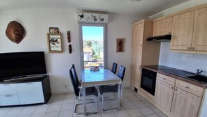A kitchen with a dining table, chairs, cabinets, and a television. - Air-conditioned 2-room apartment with a terrace, a 3-minute walk from the beach and restaurants (Cagnes-sur-Mer)