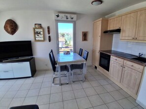 A kitchen with a dining table, chairs, cabinets, and a television. - Air-conditioned 2-room apartment with a terrace, a 3-minute walk from the beach and restaurants (Cagnes-sur-Mer)