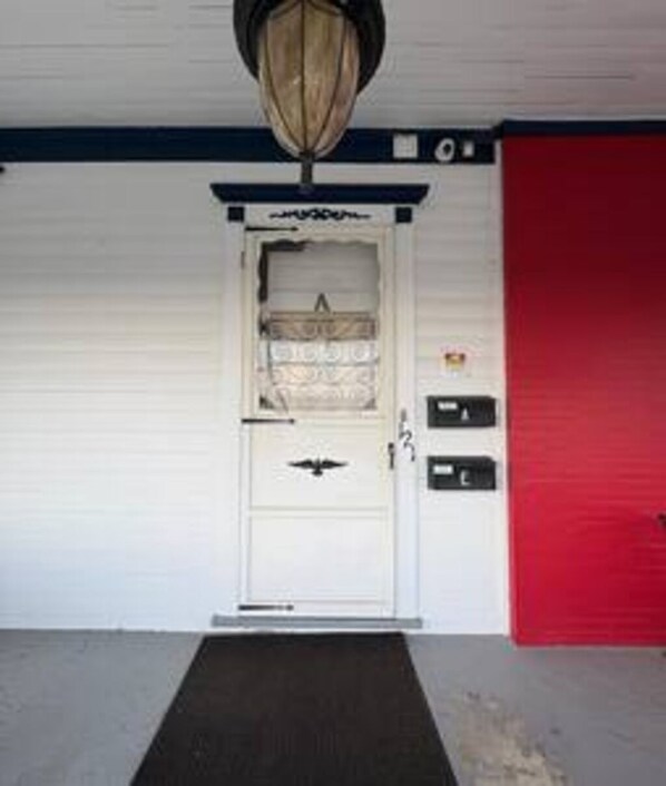 A white door with a black handle, a red door to the right, and a black mat in front. - DM-A Historic 2BR Apartment (DuBois)