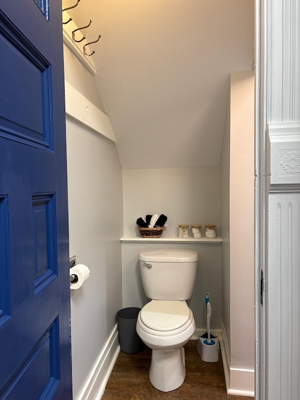 A small bathroom with a white toilet, a blue door, and a shelf with toiletries.