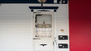 A white door with a decorative glass panel and a bird emblem, a black doormat, and a red wall to the right. - DM-A Historic 2BR Apartment (DuBois)