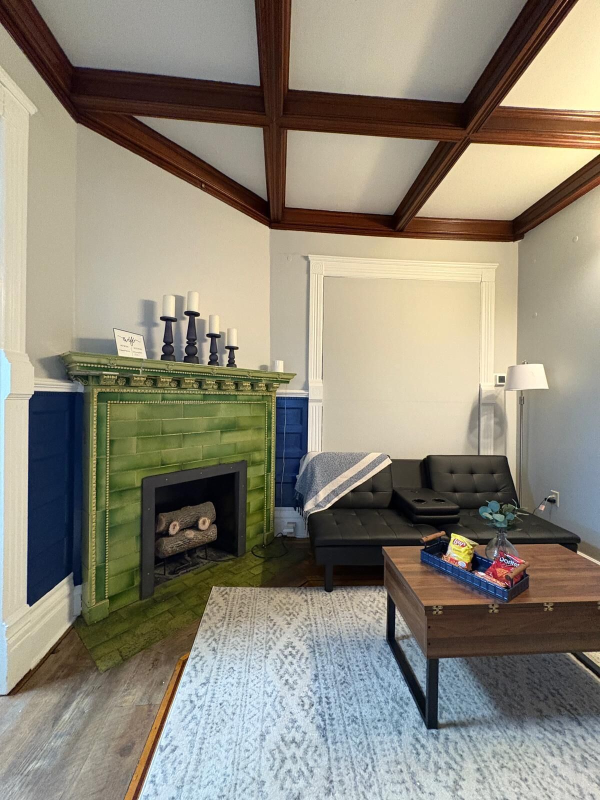 Un salon avec une cheminée verte, un canapé noir, une table basse en bois et un mur d’accent bleu.