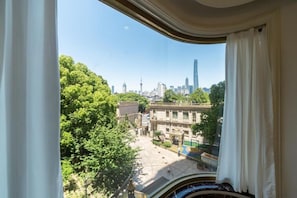 Blick aus einem Fenster mit Vorhängen auf einen Stadtblick mit Gebäuden und Bäumen.