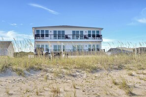 Ein zweistöckiges Gebäude mit einem Balkon im oberen Geschoss, umgeben von Sand und Gras.