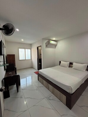 Habitación de hotel con cama, escritorio, silla, espejo, equipo de aire acondicionado y ventana.