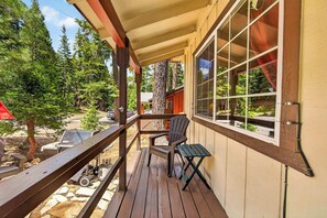 Eine Holzterrasse mit Stuhl und Tisch, eine überdachte Veranda und Blick auf einen Wald.