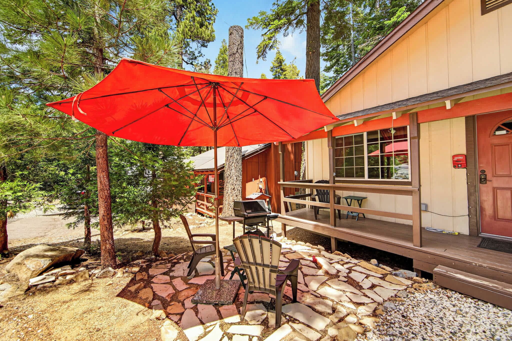 A covered outdoor seating area with a red umbrella, stone-tiled flooring, and wooden furniture.