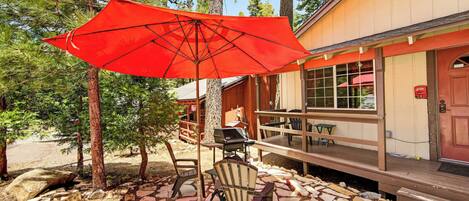 A covered outdoor seating area with a red umbrella, stone-tiled flooring, and wooden furniture.