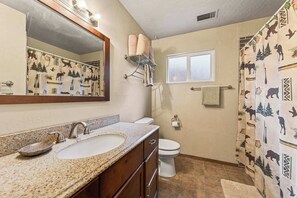 Une salle de bain avec un lavabo surmonté d’un plan de travail en granit, un miroir, des toilettes et un rideau de douche à motifs animaliers.