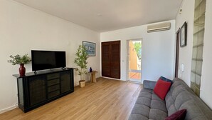 Un salon équipé d’un téléviseur à écran plat, d’un canapé, d’un plancher en bois, d’une plante en pot et d’une porte donnant sur l’extérieur.