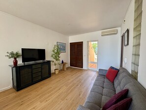 A living room with a flat-screen TV, a sofa, a wooden floor, a potted plant, and a door leading outside. - VILAMOURA MARINA VIEW 5 by HOMING (Vilamoura)