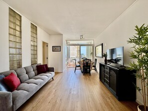 A living room with a sofa, a dining table, chairs, a TV, and a plant. - VILAMOURA MARINA VIEW 5 by HOMING (Vilamoura)
