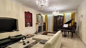 Ein Wohnzimmer mit Fernseher, einer Couch, einem Couchtisch, einem Klavier und einer Deckenleuchte.