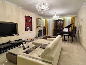 Een woonkamer met een televisie, bank, salontafel, piano en een kroonluchter.