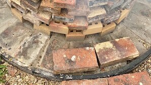 Ein runder Feuerkorb mit einer Metallschale in der Mitte, umgeben von einem Backstein-Feuerrand.