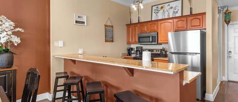 A kitchen with a central island, wooden cabinets, a stainless steel refrigerator, and a hanging light fixture.
