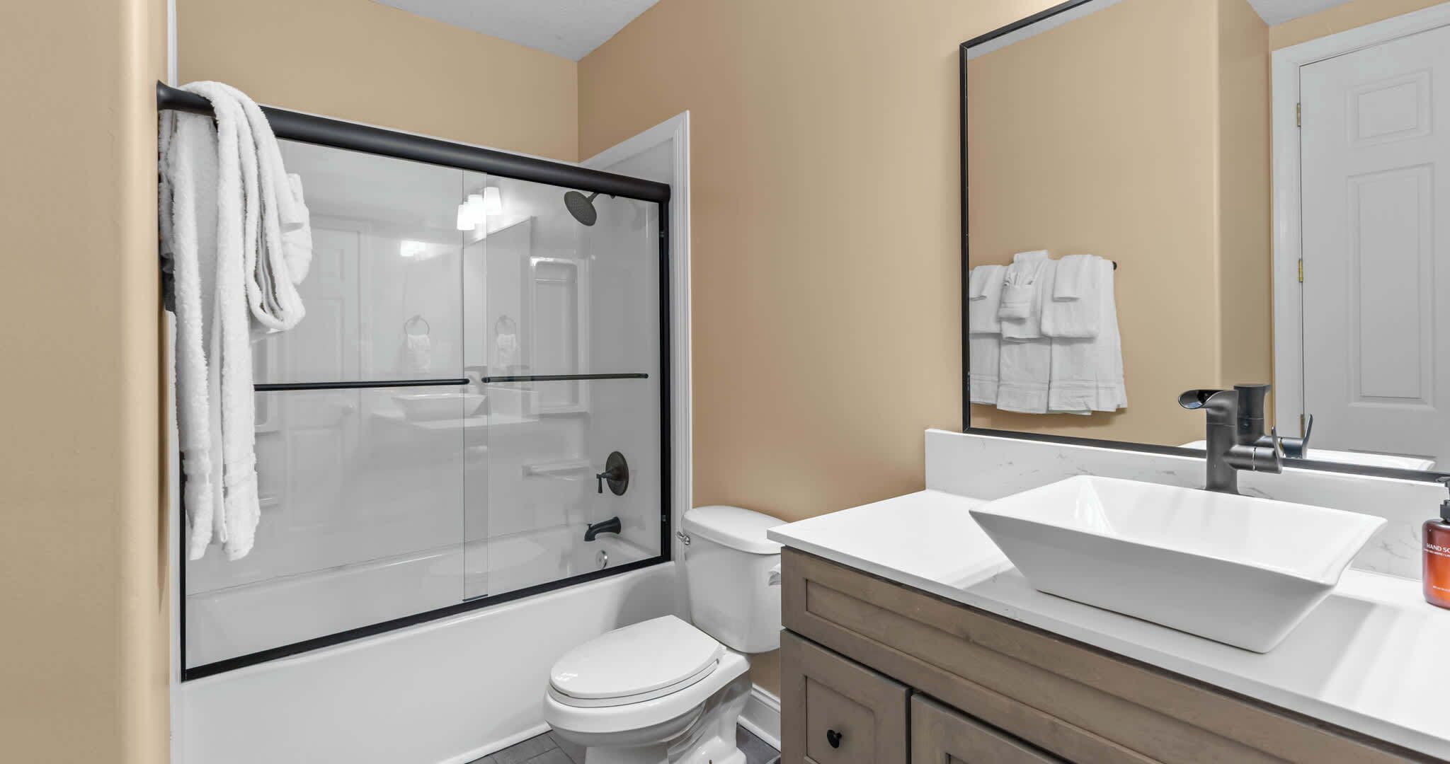 A modern bathroom with a glass shower enclosure, a white toilet, a large vessel sink, and a mirror above the sink.