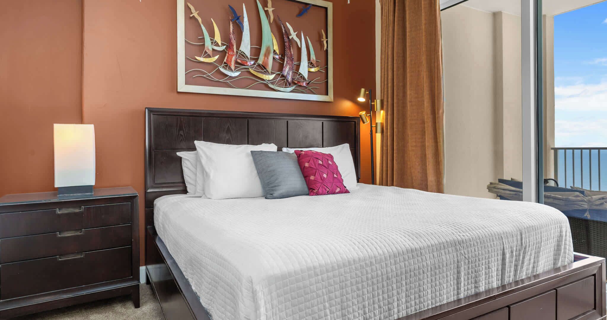 Une chambre d’hôtel avec un grand lit, une table de chevet, un tableau accroché au mur et une vue sur la mer.