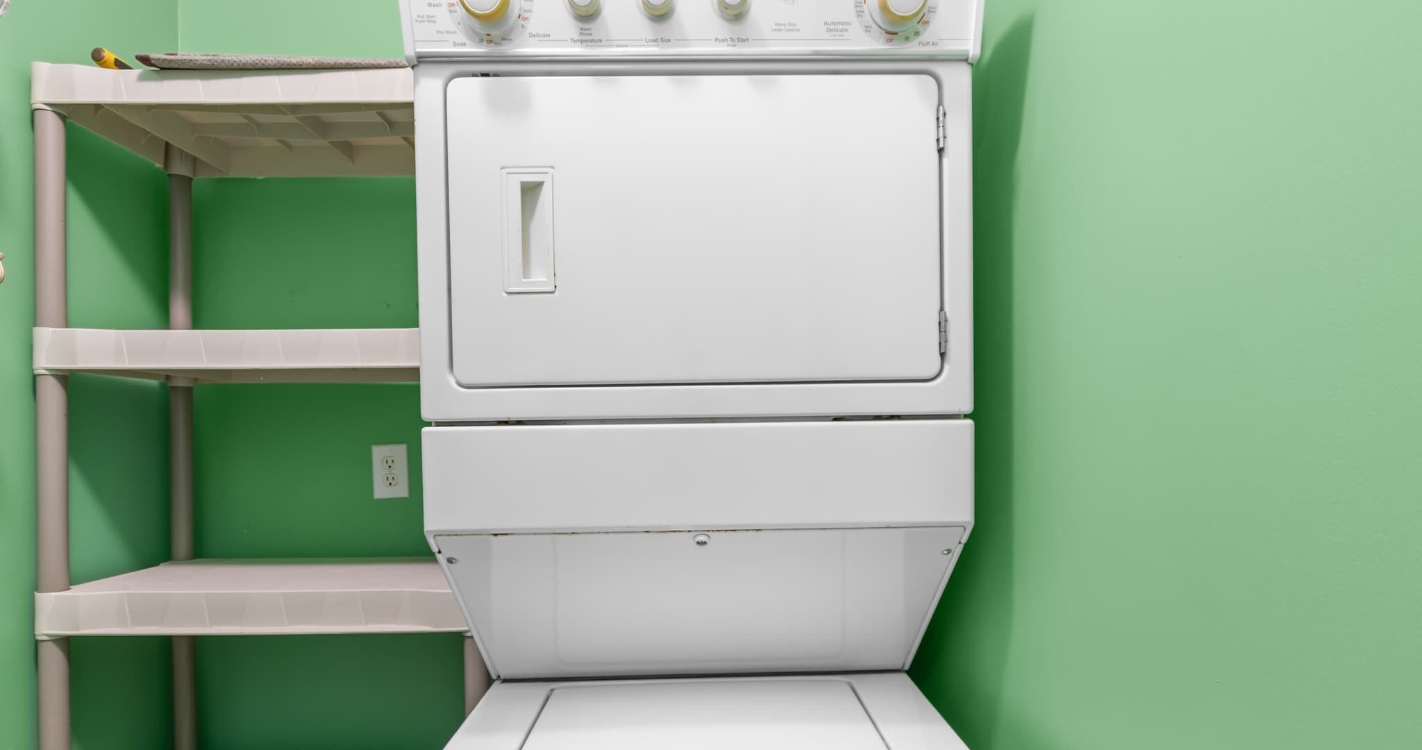 A stacked washer and dryer unit against a green wall.