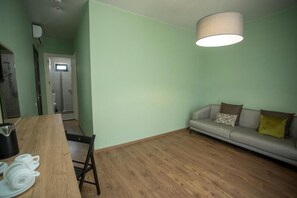 A room with a wooden floor, a sofa with cushions, a dining table with plates and a kettle, and a hanging light fixture. - Kobuleti Garden Inn (Kobuleti)