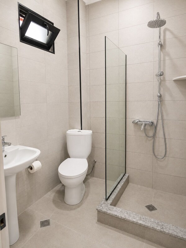 A modern bathroom with a glass shower enclosure, a white toilet, and a sink.