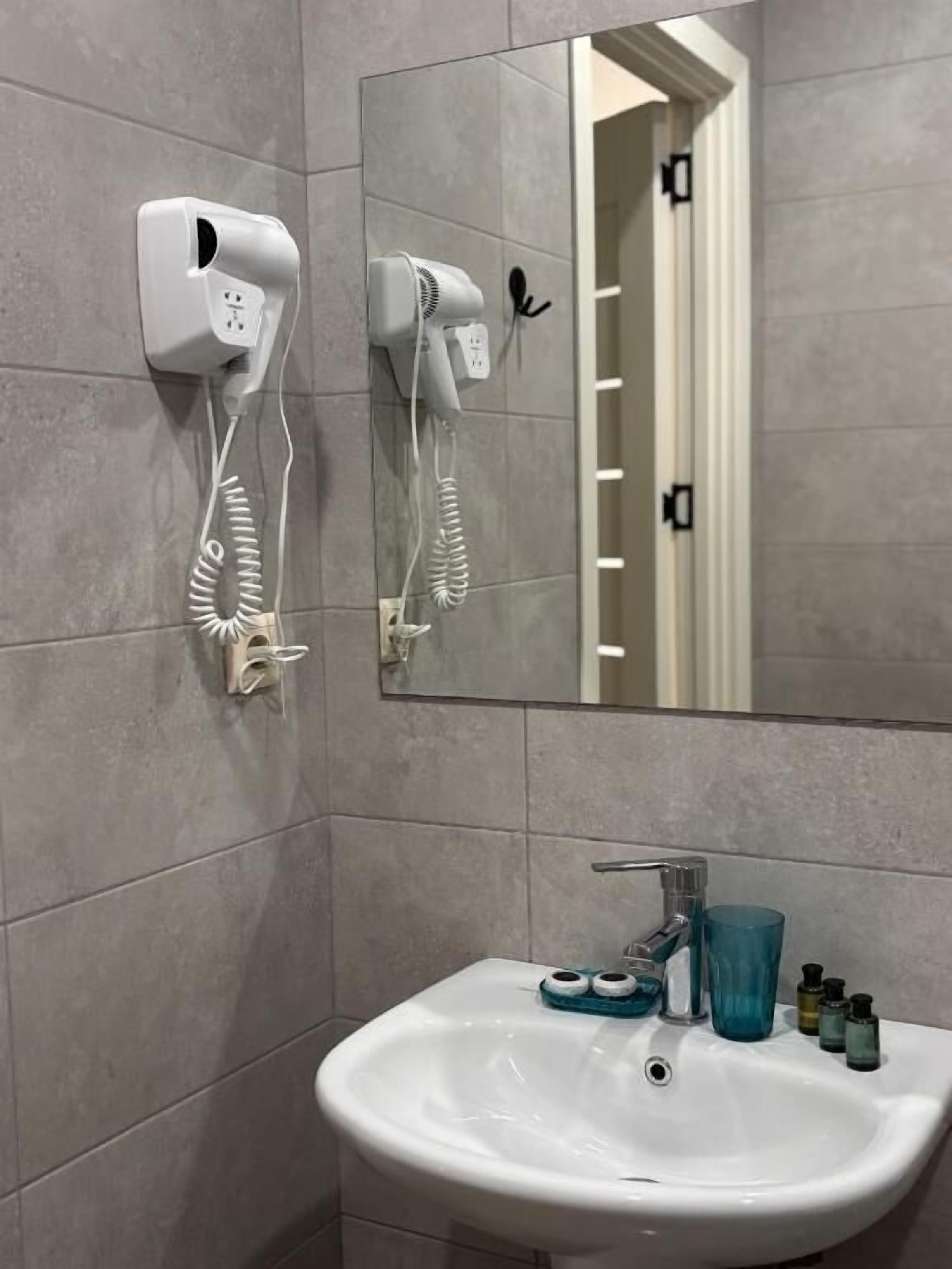 Un baño con un lavamanos blanco, un espejo y dos secadores de pelo montados en la pared.