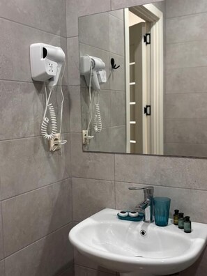 A bathroom with a white sink, a mirror, and two hair dryers mounted on the wall.