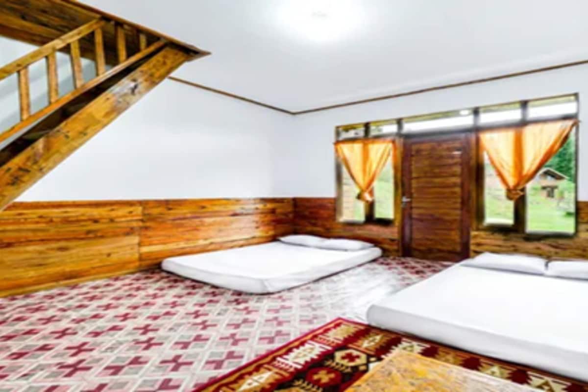 Una habitación con paredes de madera, una escalera, dos camas, un tapete estampado y una ventana con cortinas.