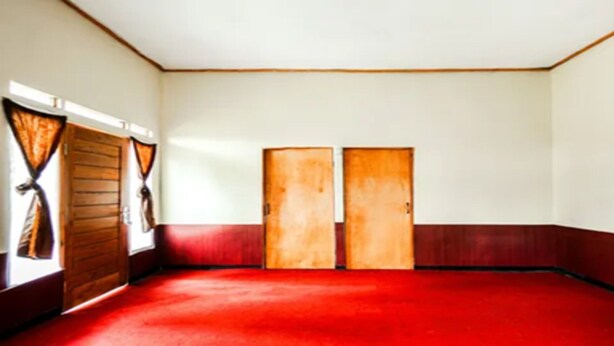 Ein Zimmer mit rotem Teppich, zwei Holztüren und einem Fenster mit Vorhängen.