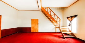 Ein Zimmer mit rotem Teppich, einer Holztreppe und einer Tür.