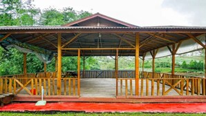 Ein hölzernes Pavillon mit einem Metall-Dach, einer Holzterrasse und roter Bodenabdeckung.