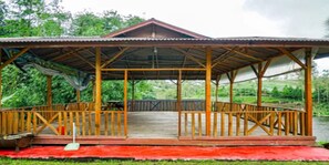 Ein hölzernes Pavillon mit einem Metall-Dach, einer Holzterrasse und roter Bodenabdeckung.