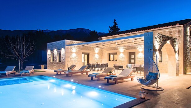 A poolside area with lounge chairs, a pool, and a stone building with outdoor lighting. - Orientem Villa Heated Pool (Nippos)