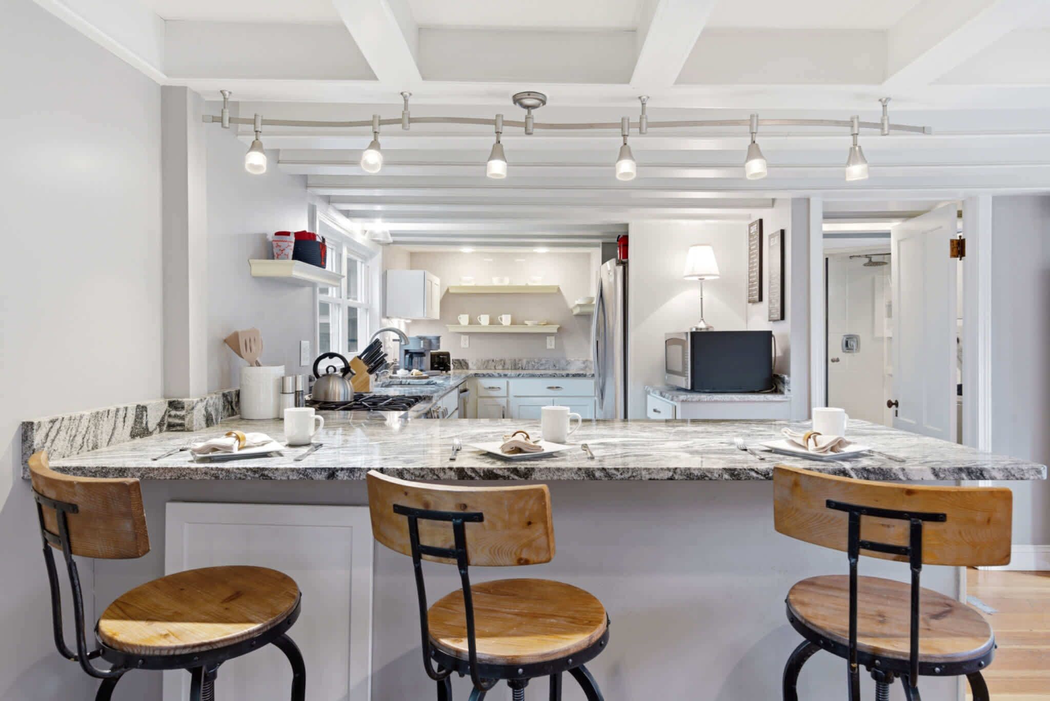 A modern kitchen with a marble countertop, wooden chairs, and a built-in island.