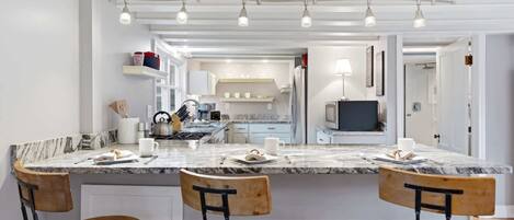 A modern kitchen with a marble countertop, wooden chairs, and a built-in island.