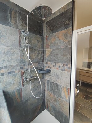 Eine Dusche mit Handbrause und Deckenbrause, ein Eckwaschbecken sowie ein gefliestes Duschgehäuse.