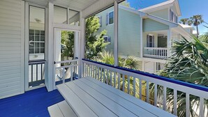 A covered porch with a bench, a white railing, and a view of a two-story house with a balcony. - Life's A Beach | Private Pool, Pet Friendly, Close to Beach (Tybee Island)