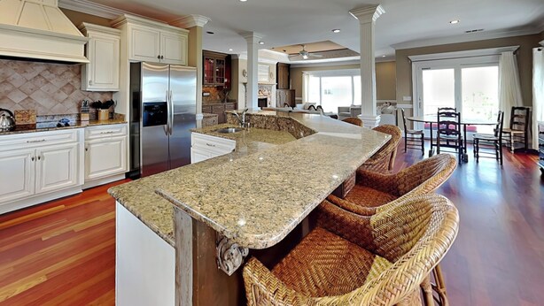 A spacious kitchen with a large island, built-in appliances, and a dining area with wicker chairs. - Tybee Nights | Great Views, Steps From Sand, Elevator (Tybee Island)