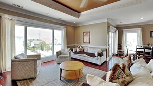 A spacious living room with large windows, a white sofa, a patterned armchair, and a round coffee table. - Tybee Nights | Great Views, Steps From Sand, Elevator (Tybee Island)