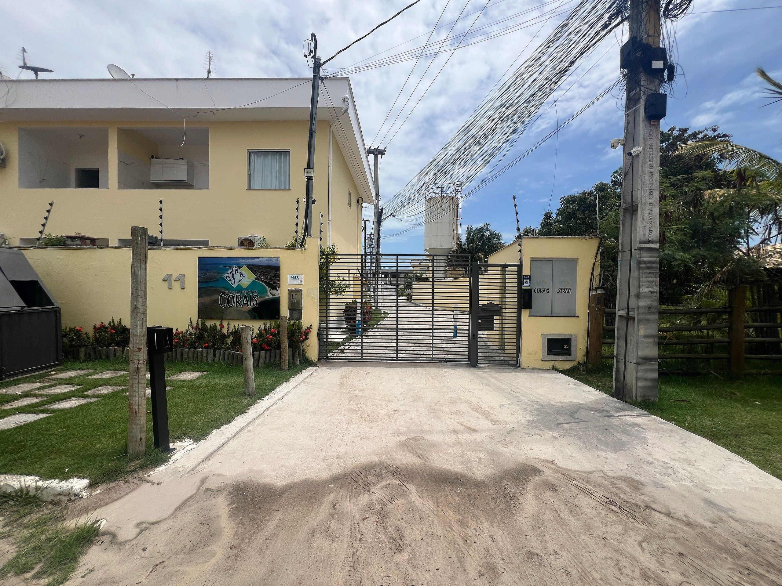 Uma entrada fechada por portão para um edifício, com uma placa indicando o nome 'CORAIS'.