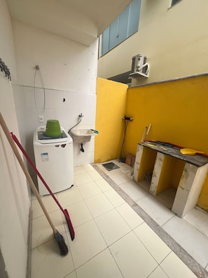 A small, compact kitchen with basic amenities including a sink, a washing machine, and a drying rack. - Residencial Praia dos Corais (Porto Seguro)