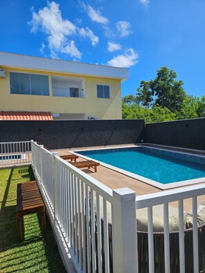 Piscina retangular com deck e cerca brancos.