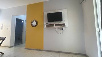 Quarto com televisão na parede, porta para outro cômodo e piso ladrilhado.