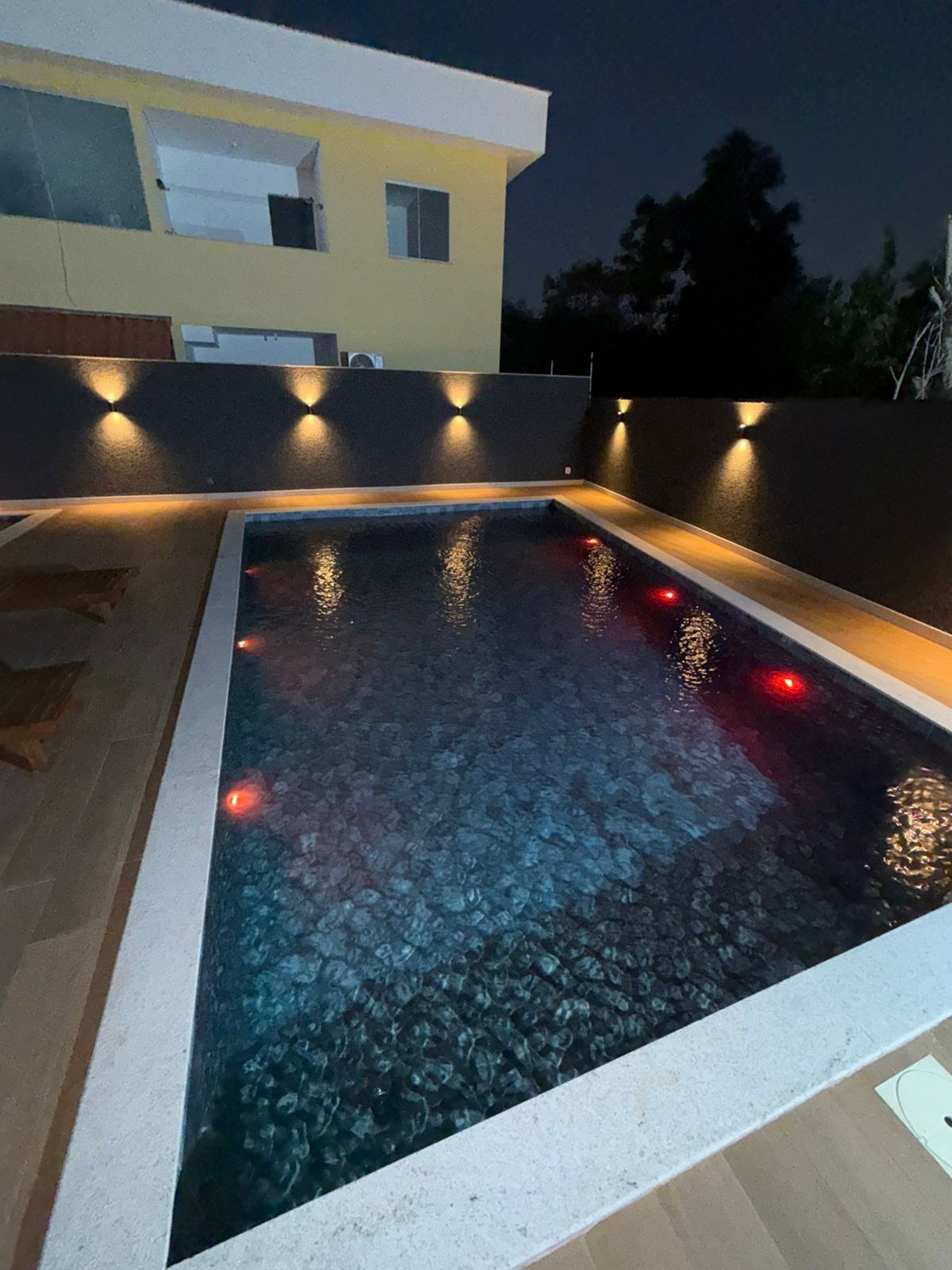 A swimming pool with a clear water surface, surrounded by a low wall and a building in the background.