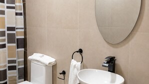 Een moderne badkamer met toilet, bidet, wastafel, spiegel en een prullenbak.