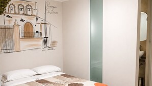 Een slaapkamer met een bed, een wanddecoratie, een badkamer zichtbaar door een open deur, en een plafondlamp.