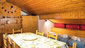 Un interno in legno con un tavolo da pranzo, sedie, un angolo cottura e una zona notte con cuscini e una valigia rossa.