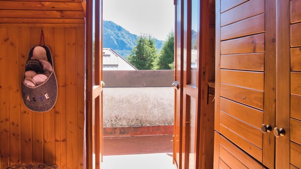 Interno in legno con un porta scarpe e vista sulle montagne attraverso una porta aperta.